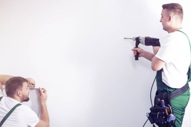 Onun iş arkadaşı bir kontur duvarla denetliyor bir bütün duvarda bir matkapla yaparken işçi. Senin boş bir duvara bir yerde