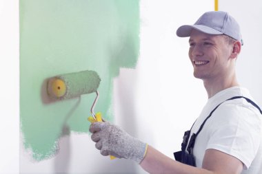 İç yeniden dekore ederken bir duvar yeşil boya silindiri ile ressam gülümseyerek