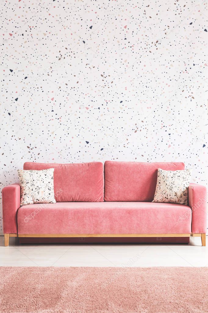 Patterned cushions on pink sofa in living room interior with carpet and lastrico wallpaper. Real photo