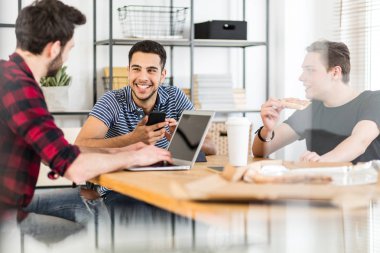 Gülümseyen adam arkadaşları pizza yemek ve bir dizüstü bilgisayarı kullanıyor smartphone kullanarak