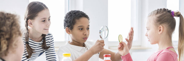 Панорама школьников, использующих увеличительное стекло для изучения кусочка огурца во время урока о здоровом питании и хороших привычках
