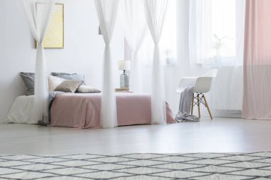 Beyaz koltuk gölgelikli pembe pastel yatak odası iç poster ve halı ile yatakta yanında. Gerçek fotoğraf