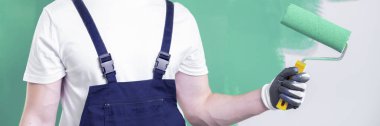 İş giysisi bezi bir neo nane boya ve bir iş-içinde-ilerleme, yeşil duvar ile arka planda tutan bir ev yenileme işçi yakın çekim
