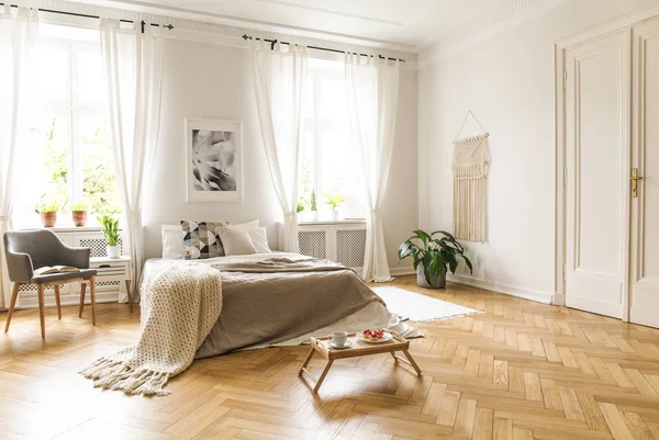 ポスターと明るい寝室のインテリアで毛布でベッドの横にある灰色のアームチェア 実際の写真 — ストック写真