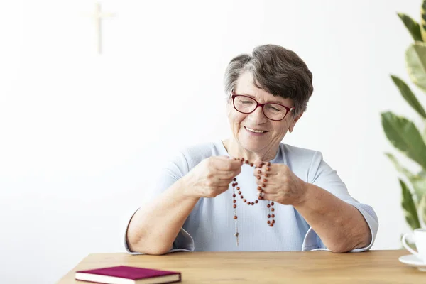 Sorrindo Mulher Idosa Segurando Rosário Enquanto Sentado Mesa Com Bíblia — Fotografia de Stock