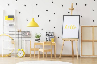 Poster mockup yanındaki küçük bir ahşap masa ve sarı süslemeleri ile SCANDI çocuk oda iç üzerine aloe tesisi