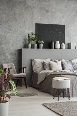 Toprak renkleri yatak odası iç bir büyük yatak, koltuk, modern rahat otel bir tabure. Siyah resim dokulu gri duvar. Gerçek fotoğraf.