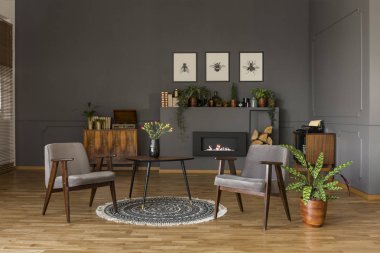 Retro oturma odası iç üretim tesisi ile gri koltuklar arasında halı üzerinde çiçekler olan tablo. Gerçek fotoğraf