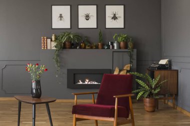 Gri oturma odası iç posterler ile çiçeklerle tablosunun yanındaki kırmızı ahşap tekli. Gerçek fotoğraf