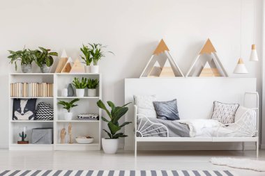 Kitap, taze bitki ve beyaz yatak odası iç metal yatağın yanındaki tüylü halı ile yastıkları ile ahşap raf