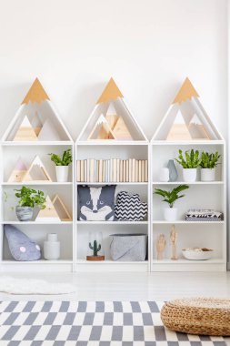 Üçgen ahşap raflar yastıklar, kitap ve beyaz İskandinav tarzı genç odası iç yerde halı ile taze yeşil bitkiler ile gerçek fotoğraf