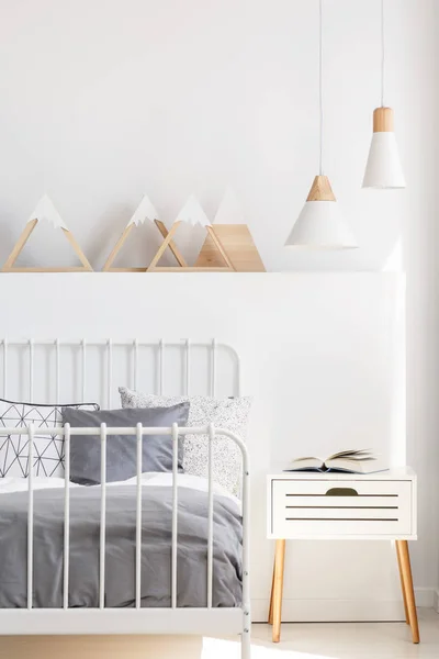 ベッドサイドの三角形の付いた白の子供の寝室のインテリアでベッドの横にあるキャビネットの上のランプです 実際の写真 — ストック写真