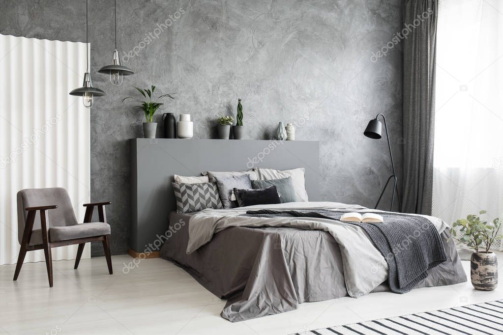 Modern grey bedroom interior with big bed with pillows and linen. Comfortable armchair next to the bed. Real photo.