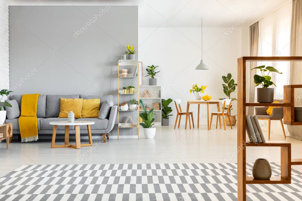 Patterned carpet and table in spacious apartment interior with yellow cushions on grey couch. Real photo