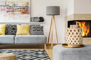 Bir kanepenin yanındaki bir lamba ve desenli bir halı ve salon iç resim ve şömine ile ahşap sepeti ile kabarık arkasında duran yastıklar gerçek fotoğraf