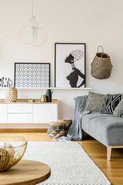 Bir kanepe yastık ve battaniye ayakta beyaz halı, posterler bir raf ve masa önünde bir boho oturma odası iç bir dolapta yanında gerçek fotoğraf