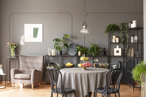 花の横にある肘掛け椅子と灰色のロフトのインテリアの果物とのラウンド テーブルで黒い椅子 実際の写真 — ストック写真
