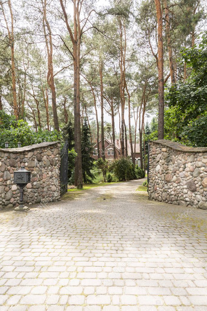Stone gate and driveway into forest with residence. Real photo
