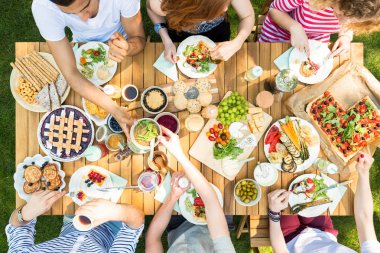 Üstten görünüm tablo pizza, pasta ve meyve ile. Açık parti sırasında öğle yemeği yiyen insanlar