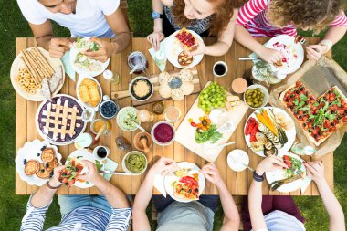 Bir grup arkadaşıyla birlikte pizza ve sebze dışında bir sıcak, güneşli gün yeme bir tahta masada oturan üstten görünüm