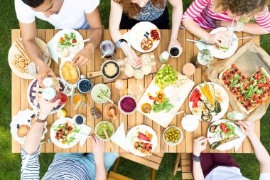 Bir grup insan konuşurken, renkli içecekler ile toasting ve vejetaryen yemek yeme ahşap bir masa etrafında oturup yüksek açı