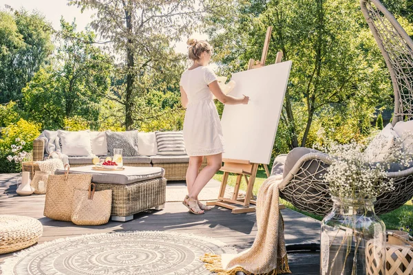 夏に庭の家具と日当たりの良いテラスで白いキャンバスに絵の若い女性 — ストック写真