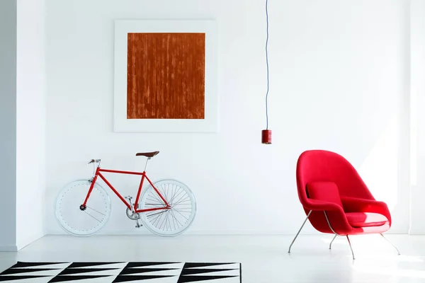 Patterned carpet and bike in white living room interior with armchair and painting. Real photo
