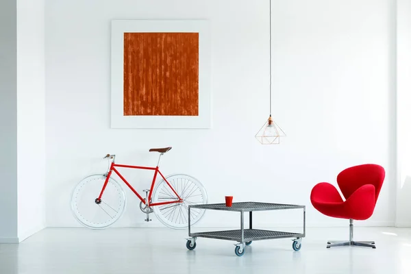 ホワイト リビング ルーム インテリア絵画と自転車の車輪の金属のテーブルの横にある赤い肘掛け椅子の立っているの実際の写真 — ストック写真