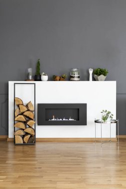 Real photo of a bio fireplace and some wood in dark, simple living room interior clipart