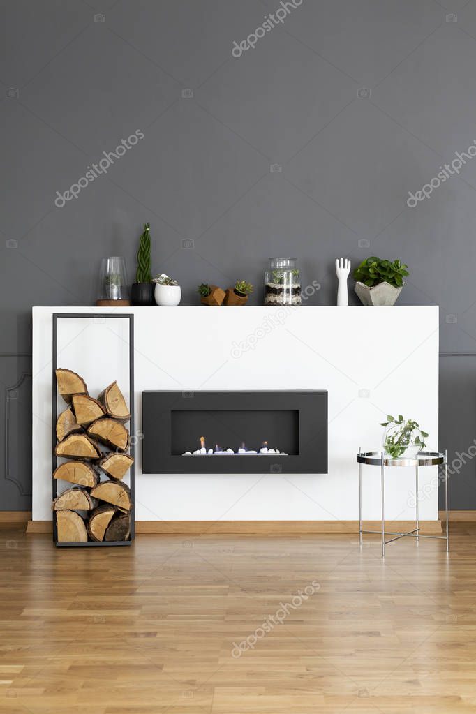 Real photo of a bio fireplace and some wood in dark, simple living room interior
