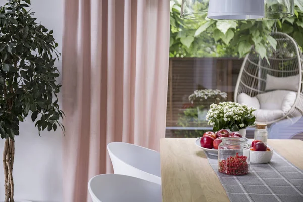 ピンクのカーテン ウィンドウのダイニング ルームのインテリアで果物を持つテーブルに白い椅子 実際の写真 — ストック写真