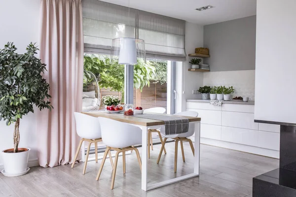 灰色罗马色调和一个粉红色的窗帘在大 玻璃窗口在现代厨房和饭厅内部与木制的桌子和白色的椅子 — 图库照片