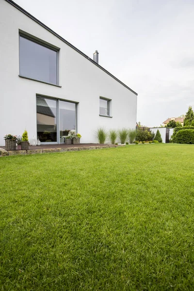 美丽的绿色草坪在一个现代住宅的后院与植物在一个木质露台和大窗户 — 图库照片