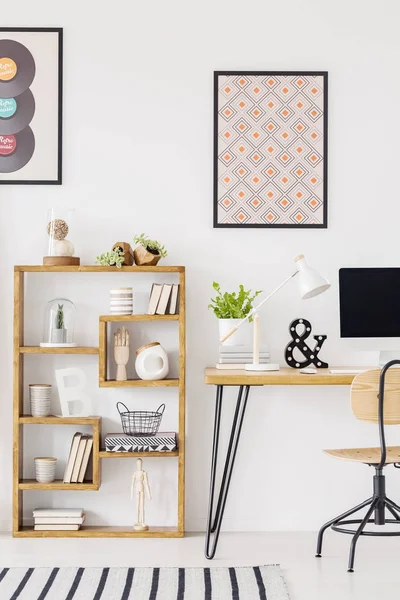 Poster above wooden desk with plant and desktop computer in home office interior. Real photo