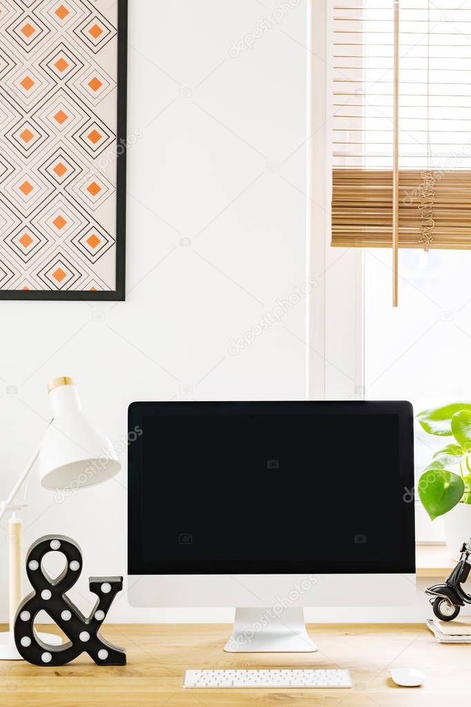 Mockup of black computer monitor on wooden desk in work area interior. Real photo with a place for your text