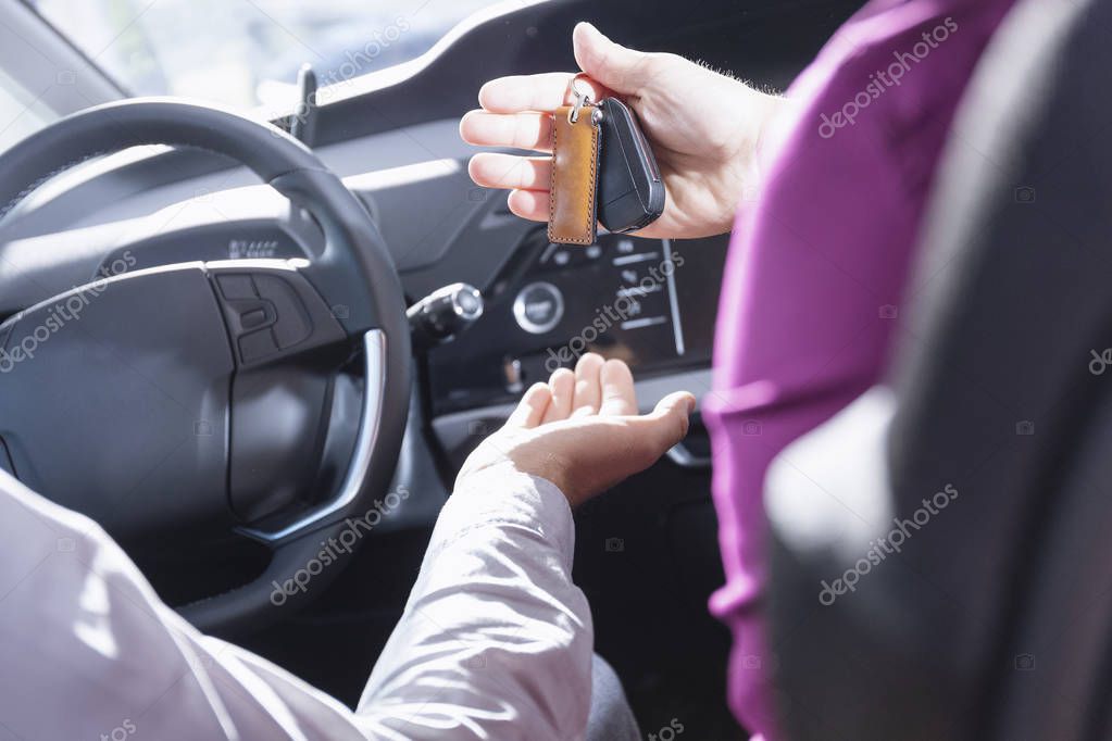 Close-up of seller giving keys to buyer during test drive in a car