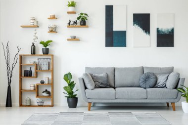 Elegant living room interior with a grey sofa, wooden shelves, plants and paintings on the wall clipart