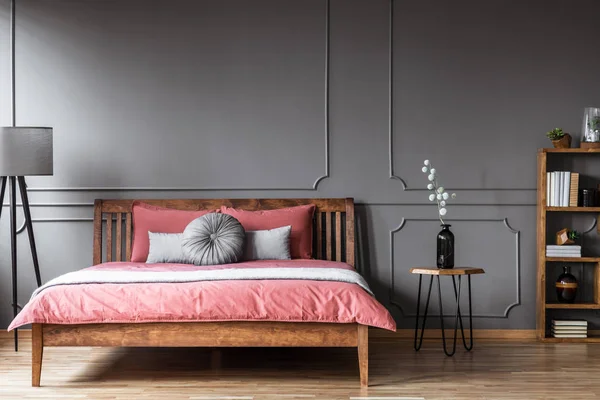 成形と壁とフェミニンな寝室のインテリアでピンクの木製ベッドの上の灰色の枕 — ストック写真