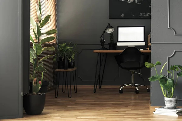 Mockup on desktop computer next to lamp in grey freelancer\'s room interior with plants. Real photo