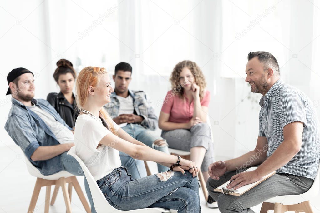 Smiling red-haired girl talking to a therapist during meeting for difficult teenagers