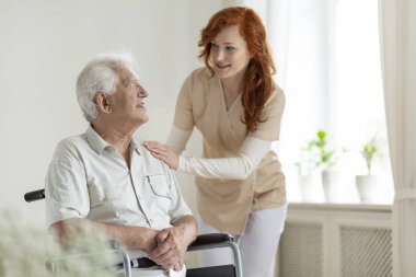 Yardım caregiver gülümseyen kıdemli adam tekerlekli sandalyede devre dışı