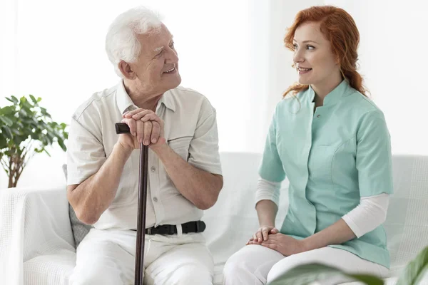 Vriendelijke Verpleegster Praten Met Lachende Oude Man Met Wandelstok — Stockfoto