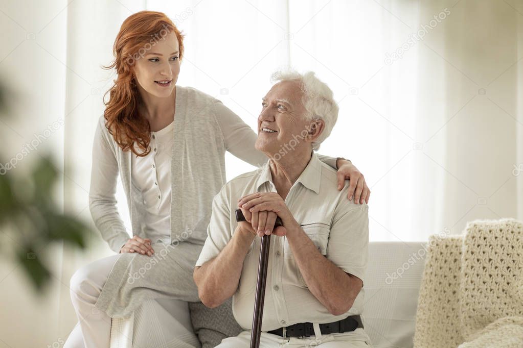 Smiling senior man with walking stick and his happy granddaughter at home