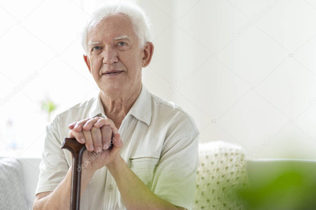 Elderly man with wooden walking stick in the nursing house