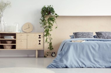 Ahşap dolap yanındaki mavi yatak yatak odası iç desenli yastıklar ile saat. Gerçek fotoğraf