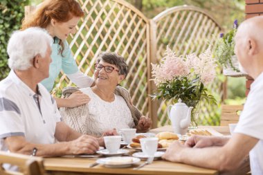 Gülümseyen yaşlı kadın arkadaşları ve onun arkasında onun caregiver ile kahvaltı