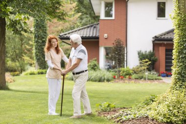 Komuta sizde baston ile bahçede destekleyen caregiver gülümseyen