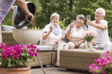 Smiling elderly people drinking wine during grill party in the garden clipart