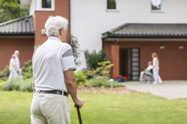 Senior man with walking stick during stay in a nursing house. Blurred background clipart