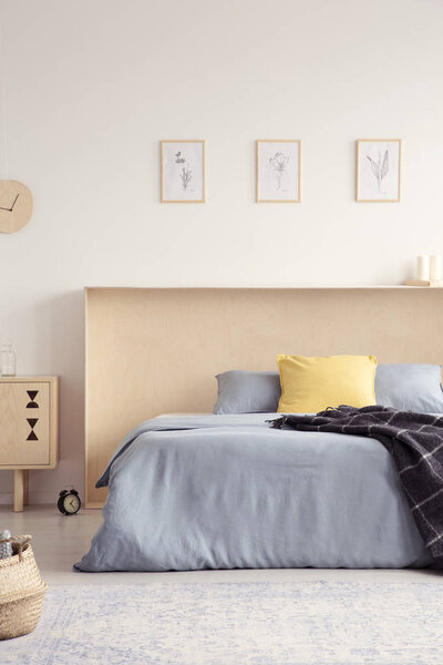 Yellow pillow and blanket on blue bed in bright bedroom interior with posters. Real photo
